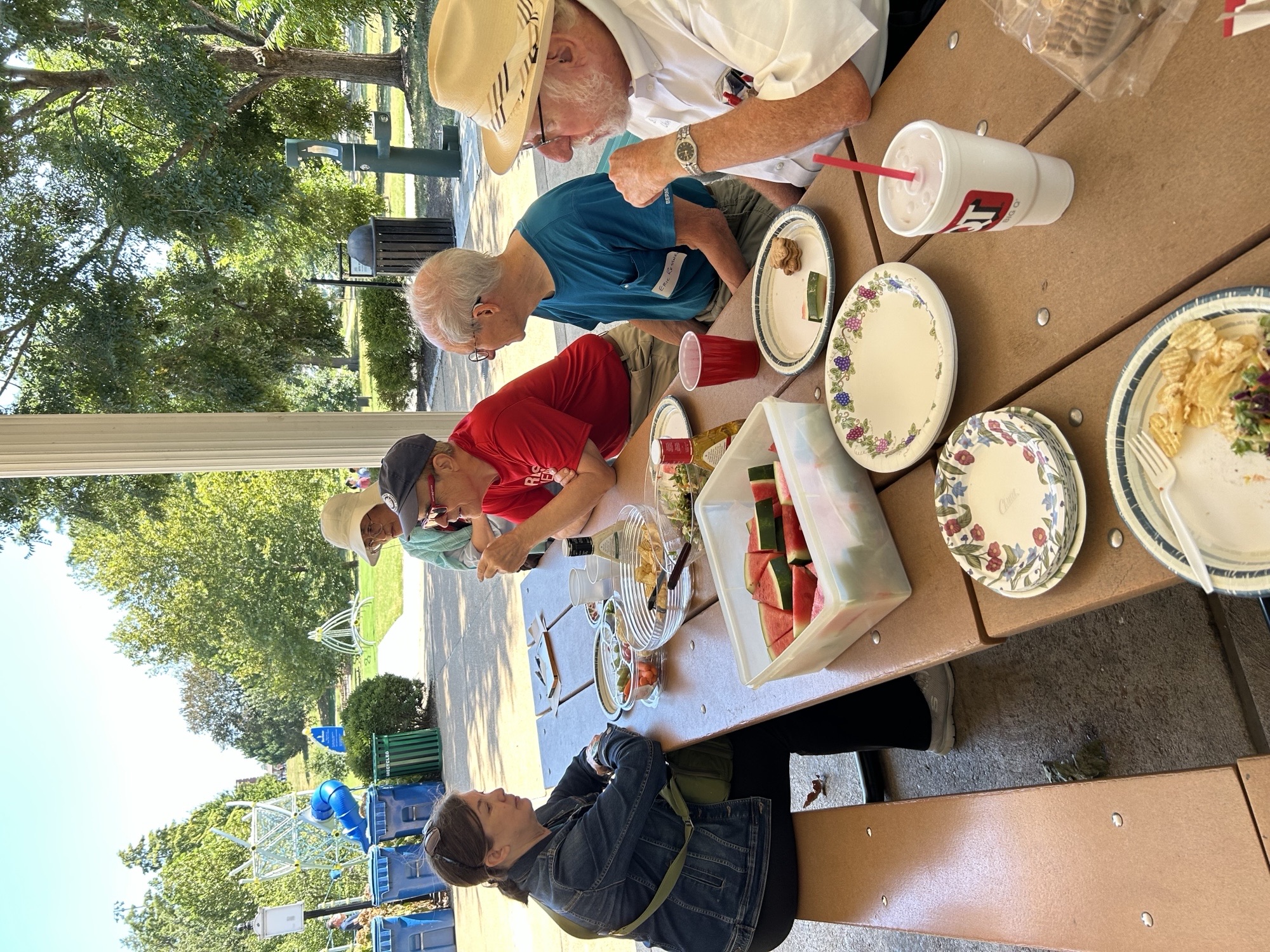 Several people sitting at a park table in a pavilion.